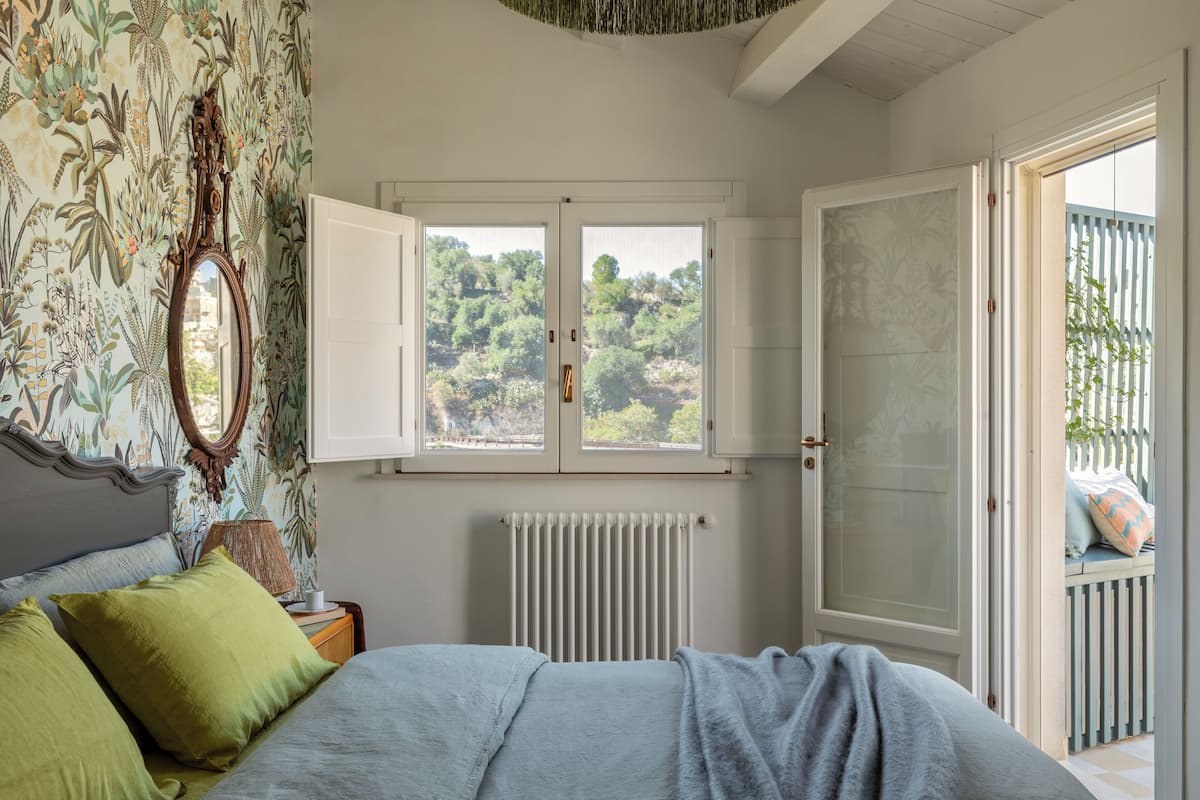 A bedroom with a bed, a window, a radiator, and a door leading to an outdoor area.