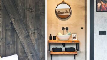 A modern bathroom with a rustic wooden door, a round mirror, a vessel sink, and a shelf with towels and a panda picture.