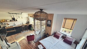 Una habitación compacta y moderna con cama, escritorio pequeño, kitchenette y ventana grande.