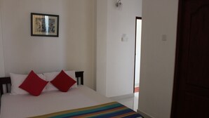 A bedroom with a bed, two red pillows, a striped blanket, a framed picture on the wall, and a wooden door. - Gerard Holiday Home (Kandy)