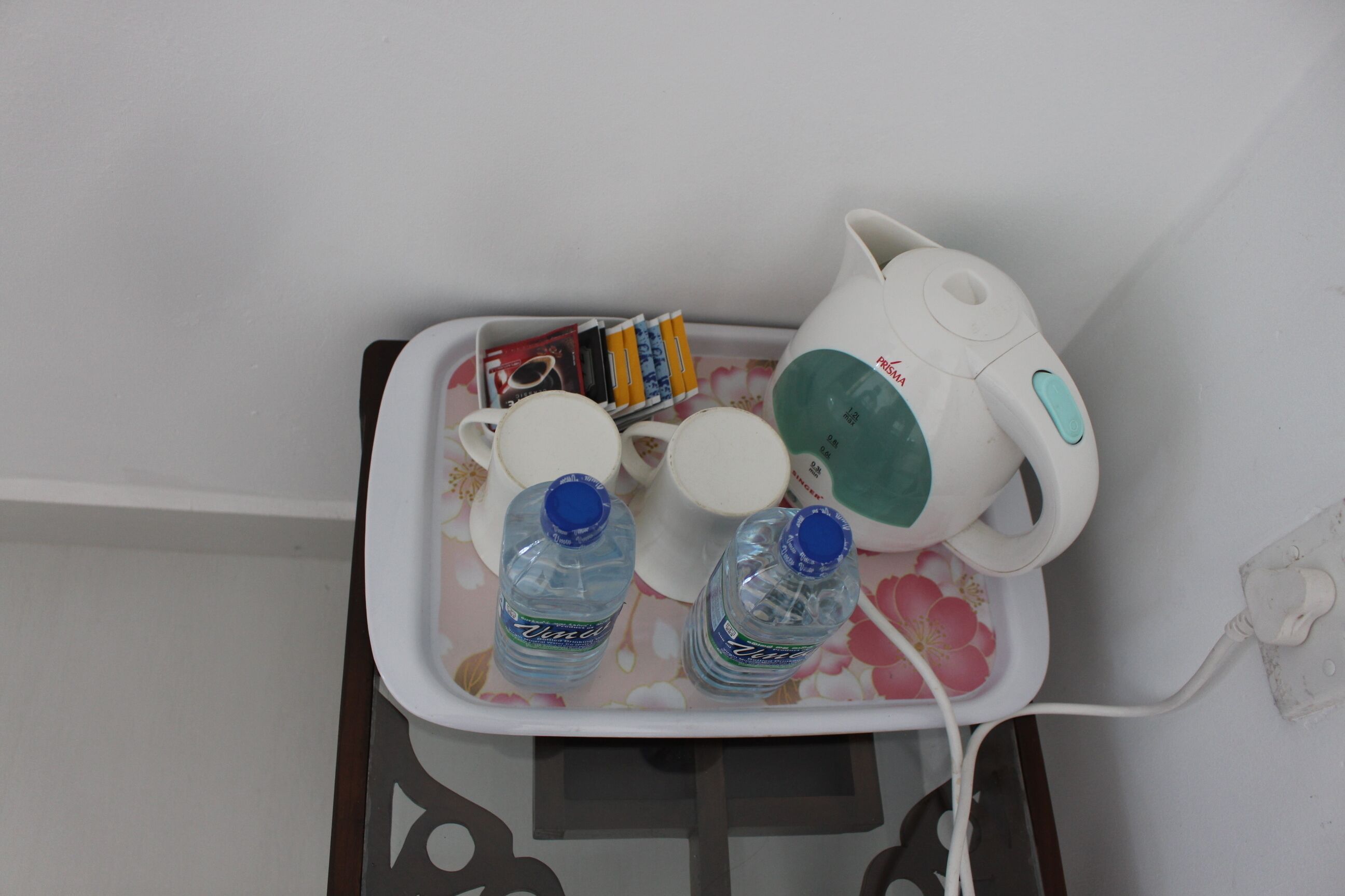 Una bandeja con una jarra de agua, dos botellas, una taza y un juego de libros sobre una mesa.
