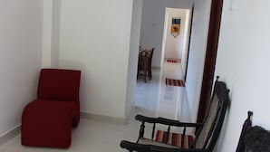A room with a red chair, a wooden chair, and a table with a striped table runner. - Gerard Holiday Home (Kandy)