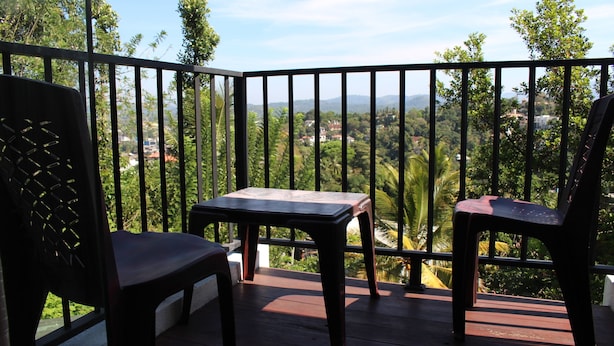 A balcony with two chairs and a table, overlooking a lush green landscape with trees and a distant view of houses. - Gerard Holiday Home (Kandy)