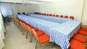 Un salón de conferencias con una larga mesa cubierta con manteles a cuadros, rodeado de sillas rojas.