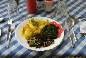 A plate of food with chips, greens, and tomatoes on a table with a checkered tablecloth. - Oyugis Hill Breeze Hotel (Oyugis)