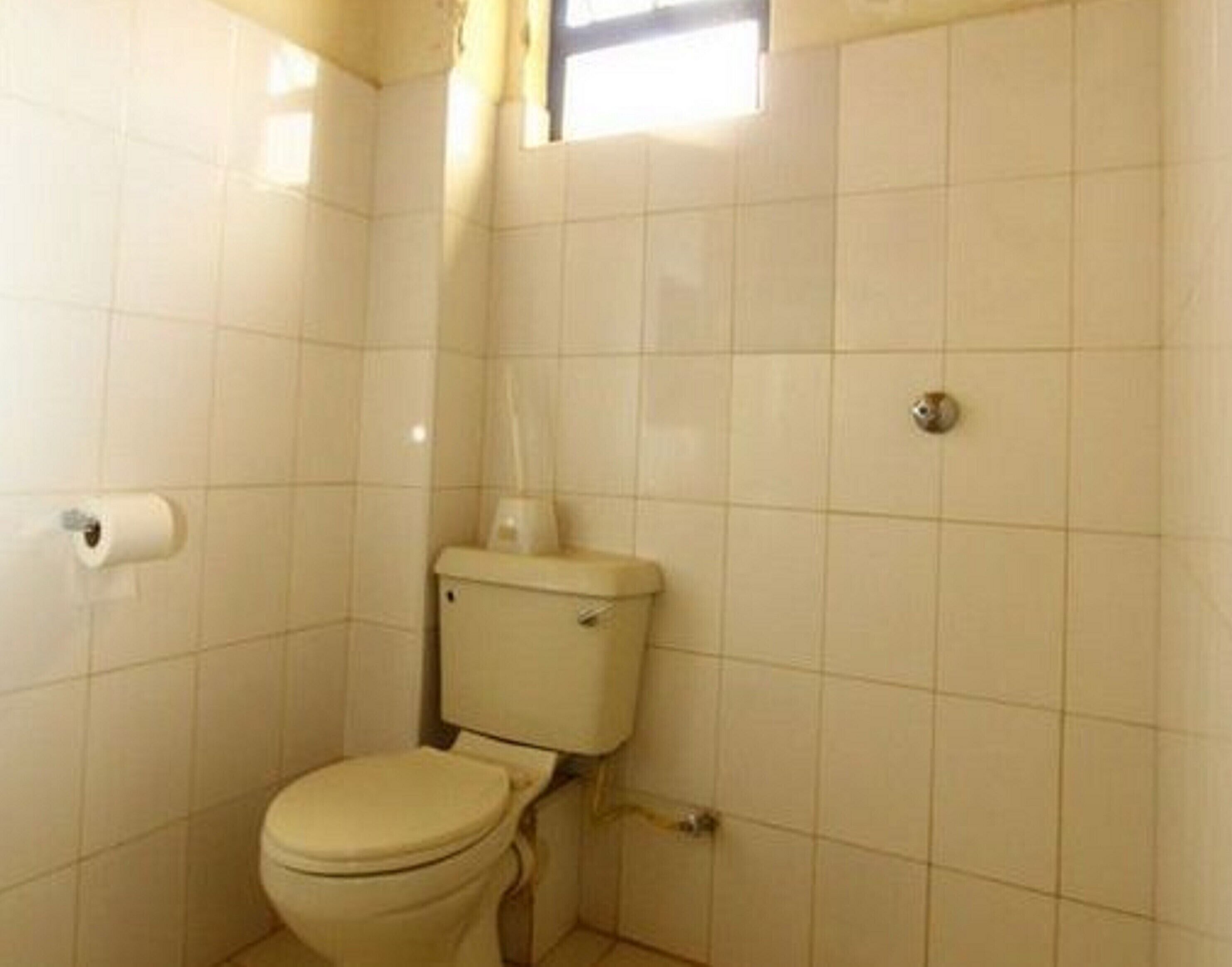 A small, basic bathroom with a toilet, a roll of toilet paper, and a window.