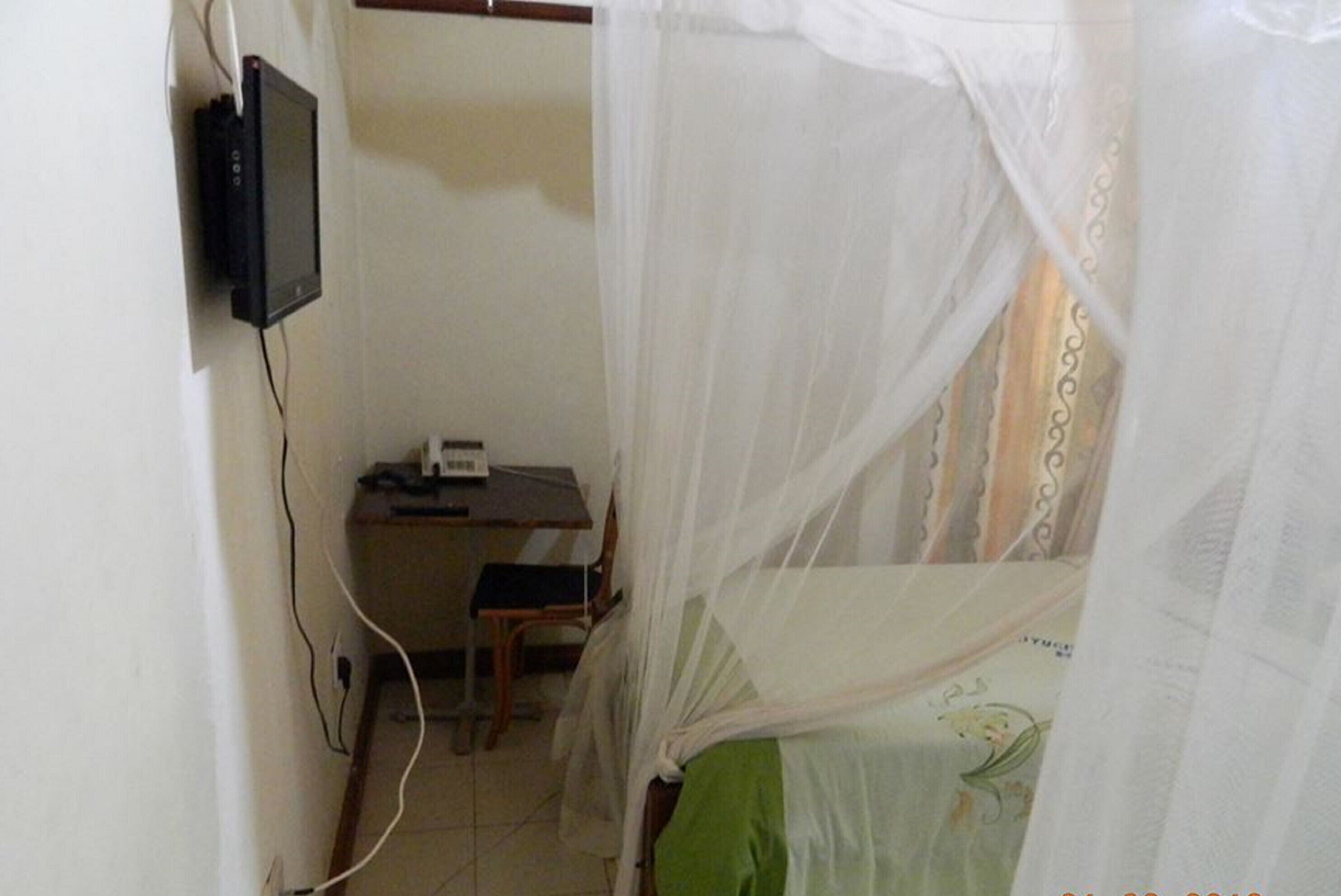 Una habitación con una cama cubierta por un mosquitero, un escritorio con un ordenador y un televisor instalado en la pared.