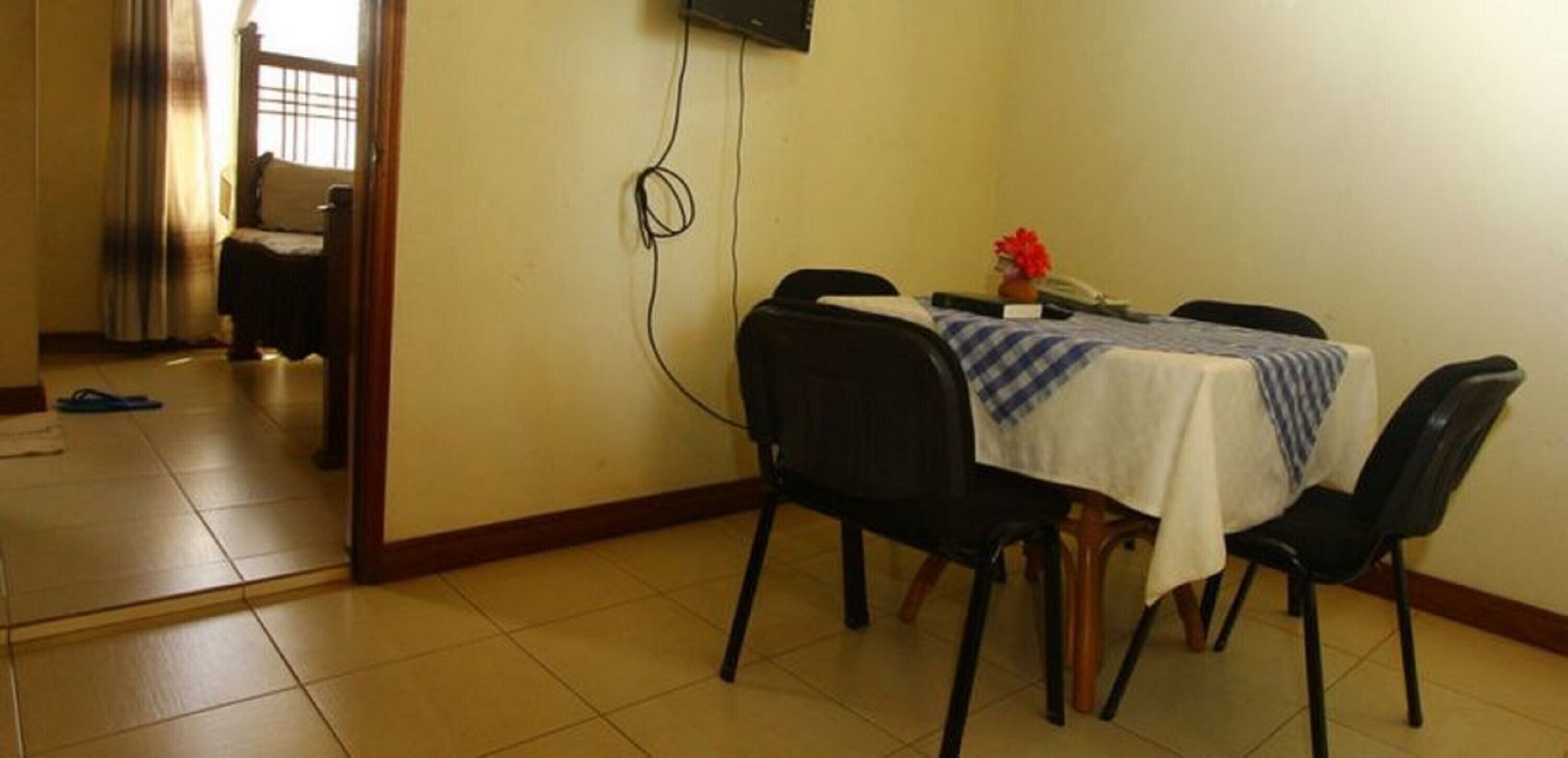 Un coin repas avec une table dressée pour quatre personnes, des chaises, un téléviseur fixé au mur et une porte donnant sur une autre pièce.