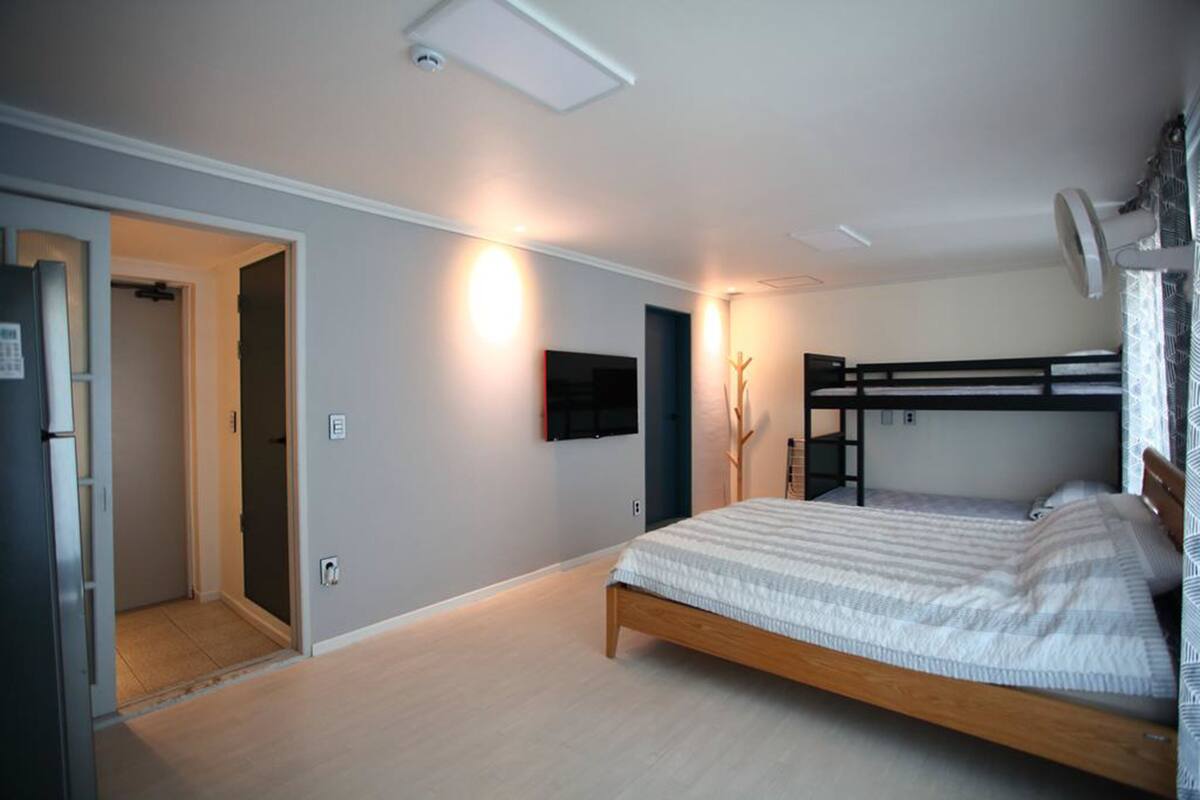 A bedroom with a bunk bed, a door leading to another room, and a wall-mounted TV.