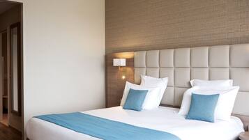 A hotel room with a large bed, a headboard with a light fixture, and a wooden floor.