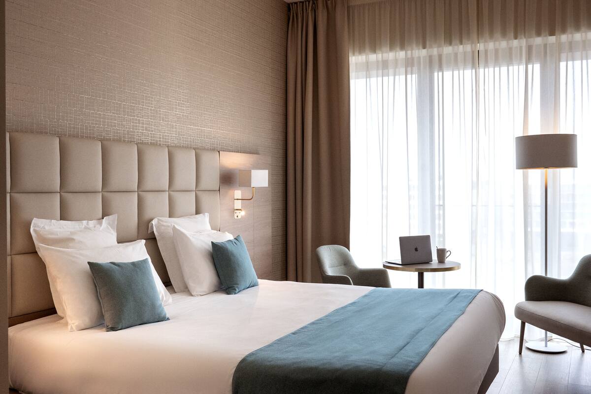 Habitación de hotel con una cama grande, cabecera con iluminación integrada, un escritorio con una computadora portátil y una silla.