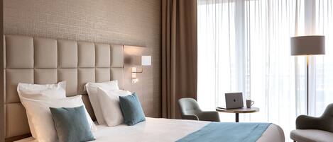 Habitación de hotel con una cama grande, cabecera con iluminación integrada, un escritorio con una computadora portátil y una silla.