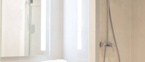 Un baño moderno con un espejo grande, un lavamanos, un perchero para toallas y una ducha con cabezal de ducha de mano.