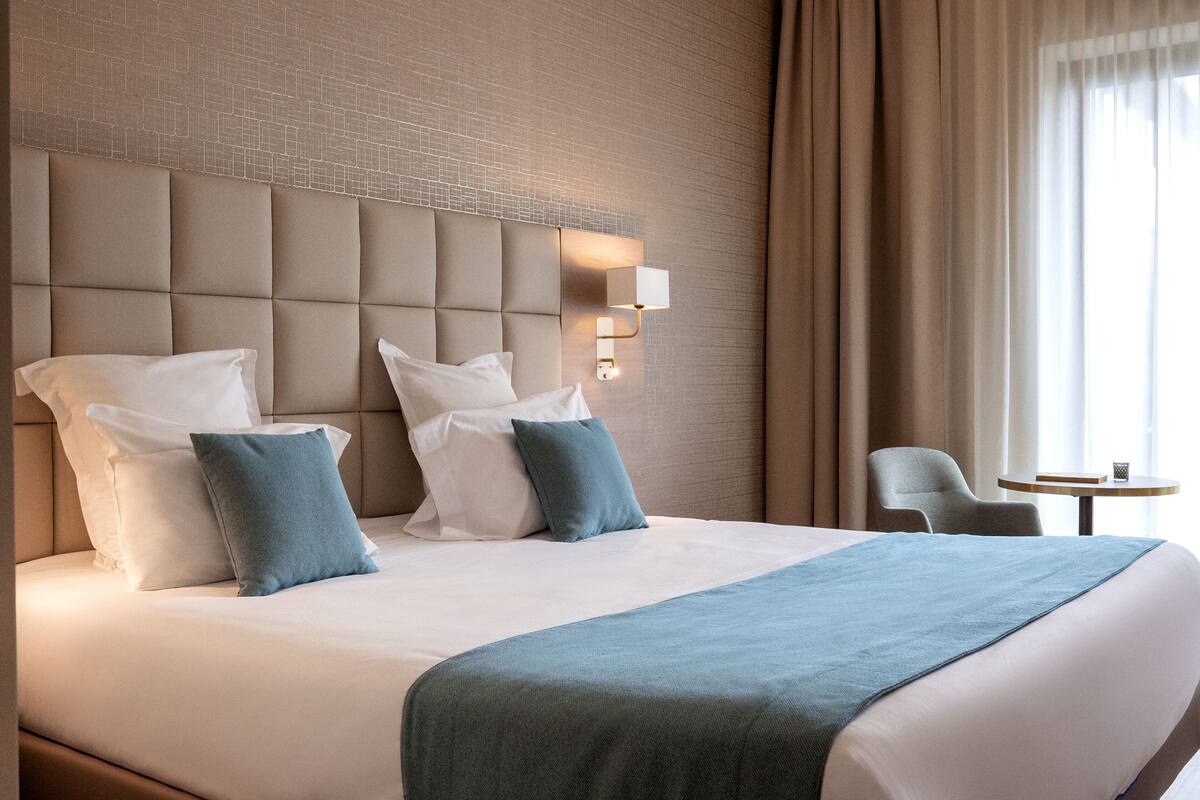 Habitación de hotel con una cama grande, cabecera con lámpara, una silla y una mesita.