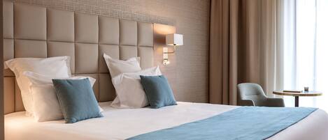 A hotel room with a large bed, a headboard with a light fixture, a chair, and a small table.