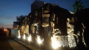 A rock formation with embedded lights, a building in the background, and a palm tree.