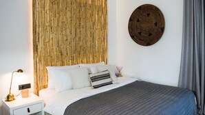 Et moderne soveværelse med en vægpanel i bambus, vægkunst i flettet design, en seng med hvidt og mønstret sengetøj og et natbord med en lampe.