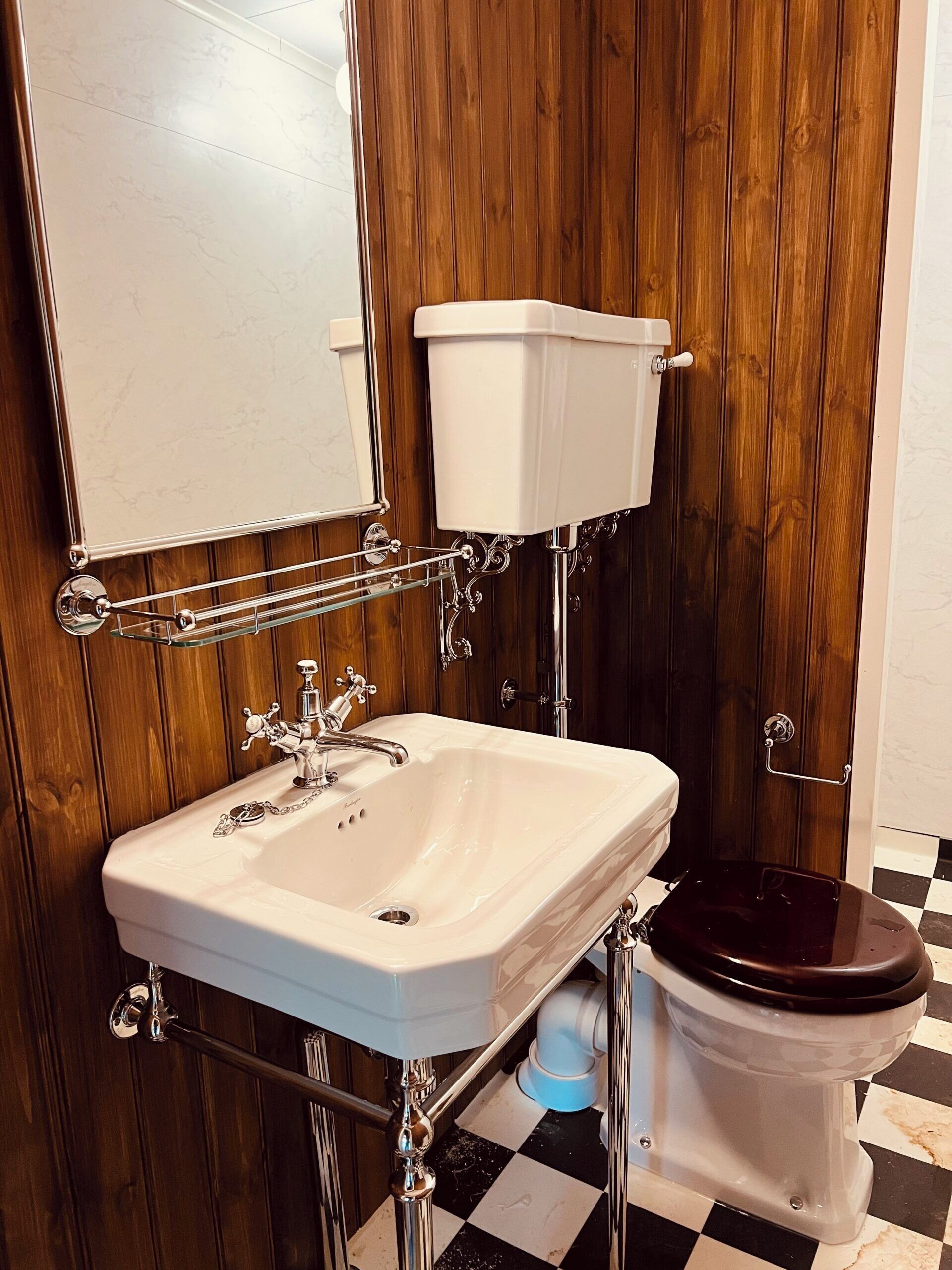 Een badkamer met een wit wastafel, houten paneelwanden, een toilet en een spiegel.