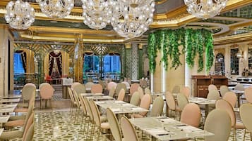 A luxurious dining area with ornate chandeliers, a patterned floor, and a green wall with hanging plants.