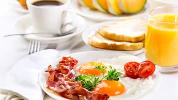 Un plato de desayuno con huevos, tocino, tomates, una taza de café, tostadas y un vaso de zumo de naranja.