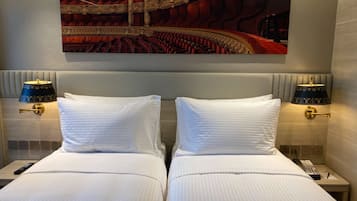 Una habitación de hotel con dos camas, un cuadro grande de una ópera y lámparas de noche.