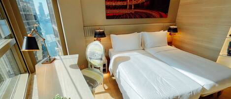 Ein modernes Hotelzimmer mit einem großen Bett, Nachttischlampen, einem kleinen Tisch mit Pflanze und Blick auf die Stadt durch das Fenster.
