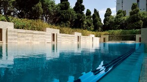 A swimming pool with clear blue water, surrounded by a stone wall and greenery. - Hotel Alexandra (Hong Kong)