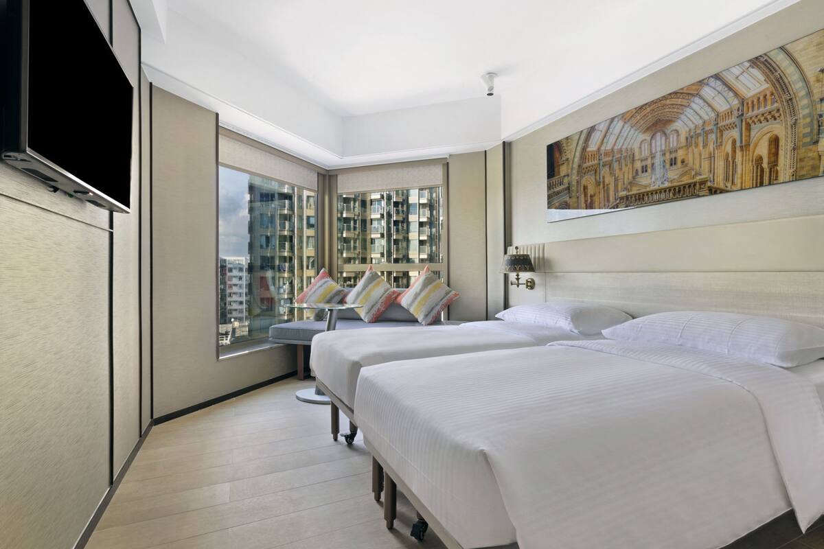 A hotel room with two beds, a large window with a city view, a painting on the wall, and a flat-screen TV.