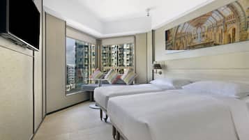 A hotel room with two beds, a large window with a city view, a painting on the wall, and a flat-screen TV.