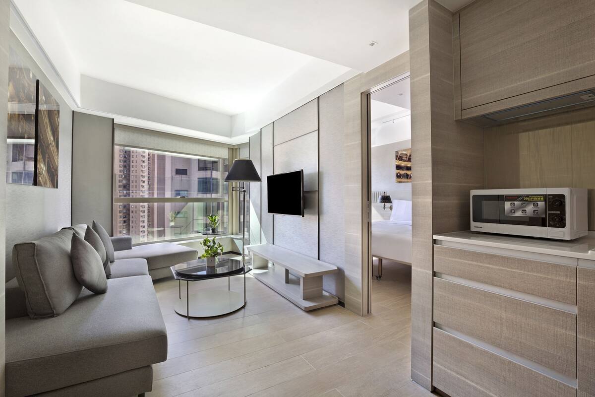 A modern living room with a sofa, a coffee table, a flat-screen TV, and a microwave.