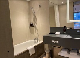 Un baño moderno con bañera, ducha, tocador con espejo y un perchero para toallas.