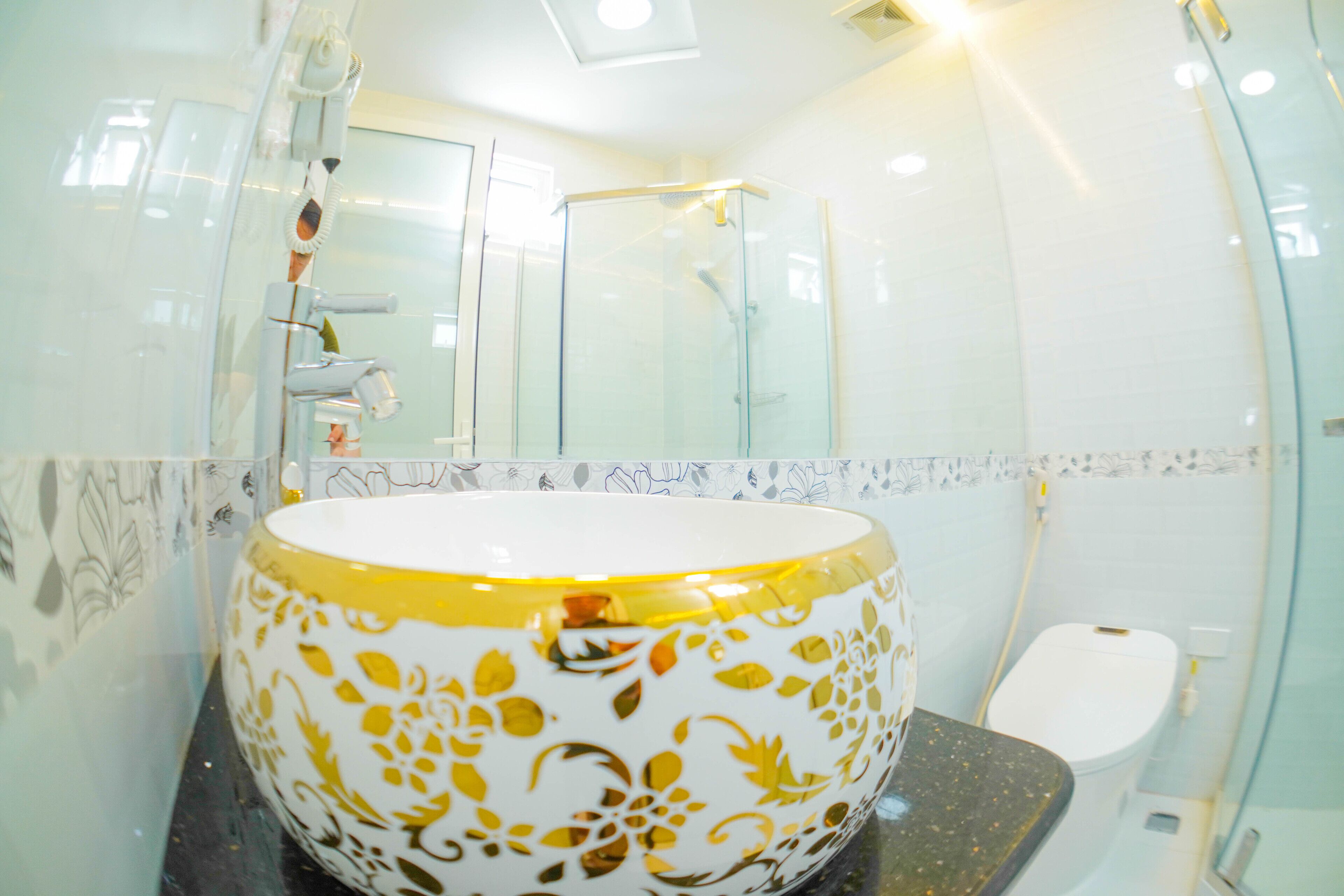 Ein Badezimmer mit einem großen, weißgoldenen Waschbecken, einer Duschkabine aus Glas und einer weißen Toilette.