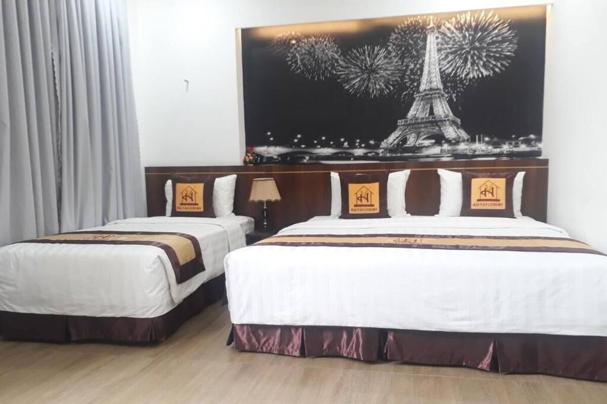 A hotel room with two beds, a large painting of the Eiffel Tower, and a wooden floor.