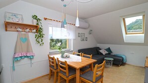 A cozy dining area with a wooden table and chairs, a window with a view of greenery, and a ceiling fan. - Apartments Laznica (Cerkno)