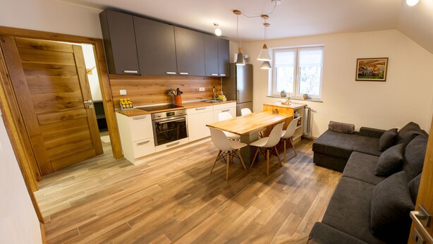 A modern kitchen with dark cabinets, a wooden dining table, and a gray sofa. - Apartments Laznica (Cerkno)