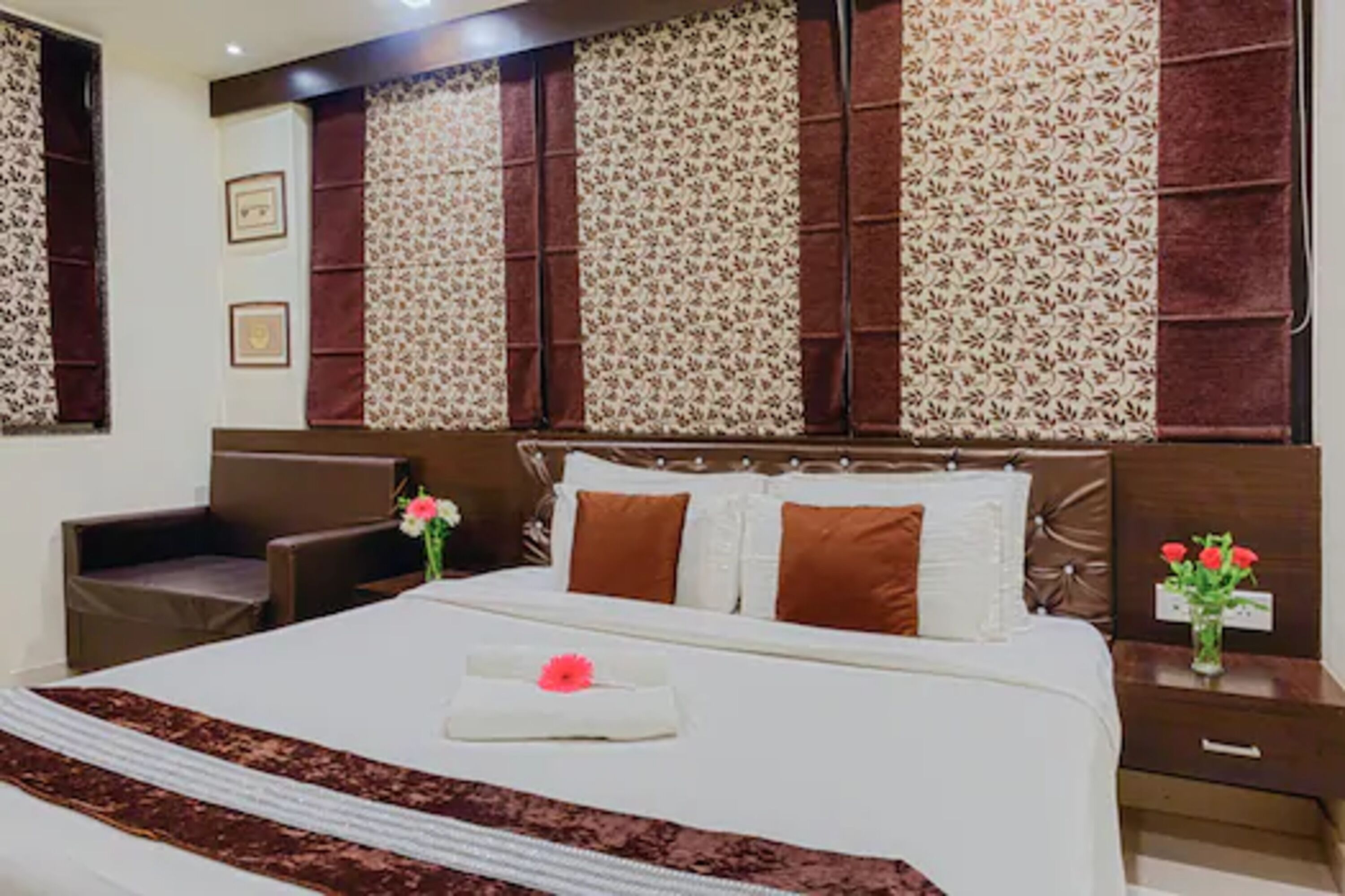 Una camera d'albergo con un letto grande, un comodino con un vaso di fiori e una sedia.