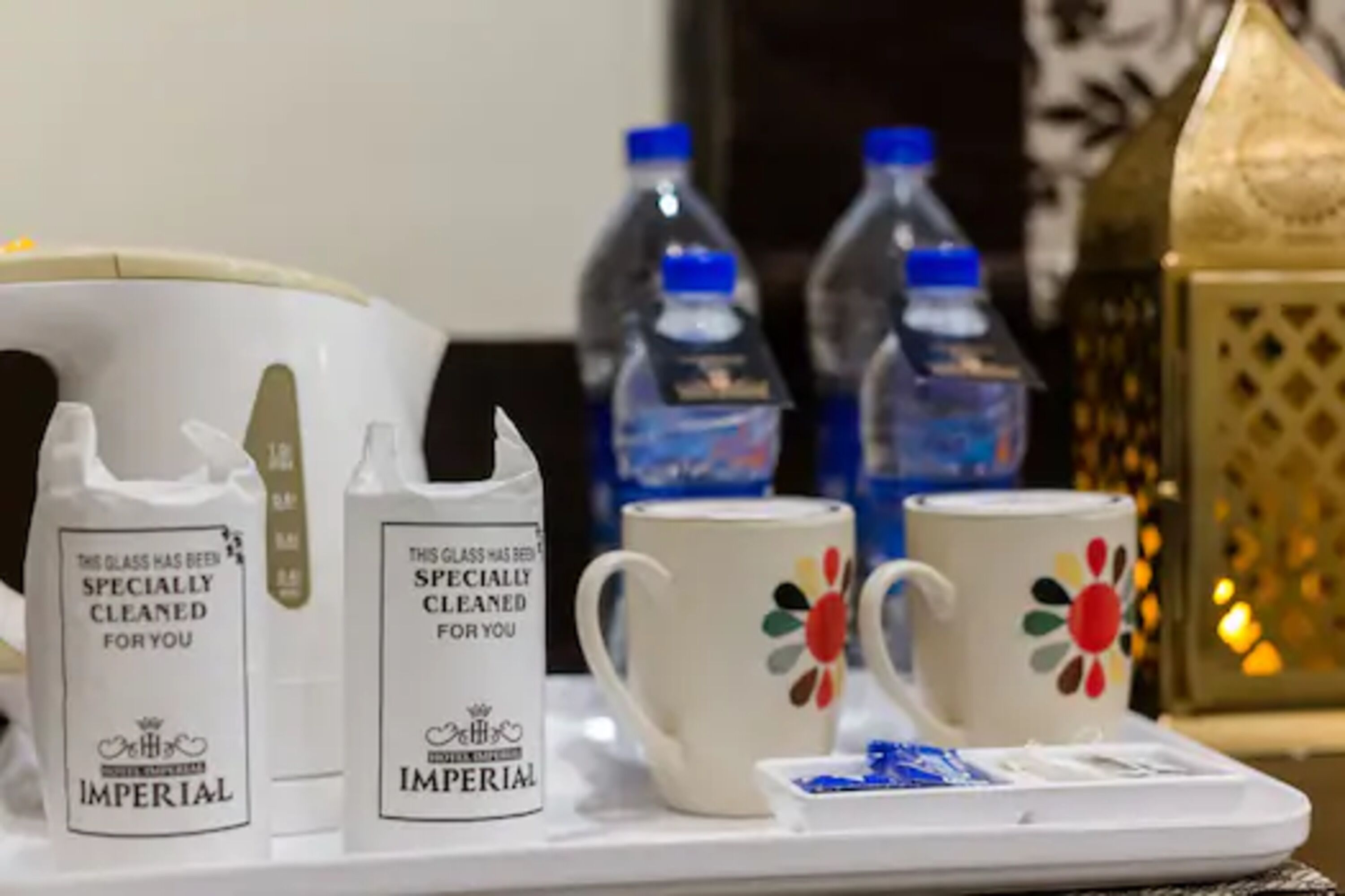 Un plateau contenant deux produits de nettoyage pour vitres de la marque Imperial, deux tasses blanches ornées de motifs floraux colorés et un petit plateau de sucres en morceaux bleus.