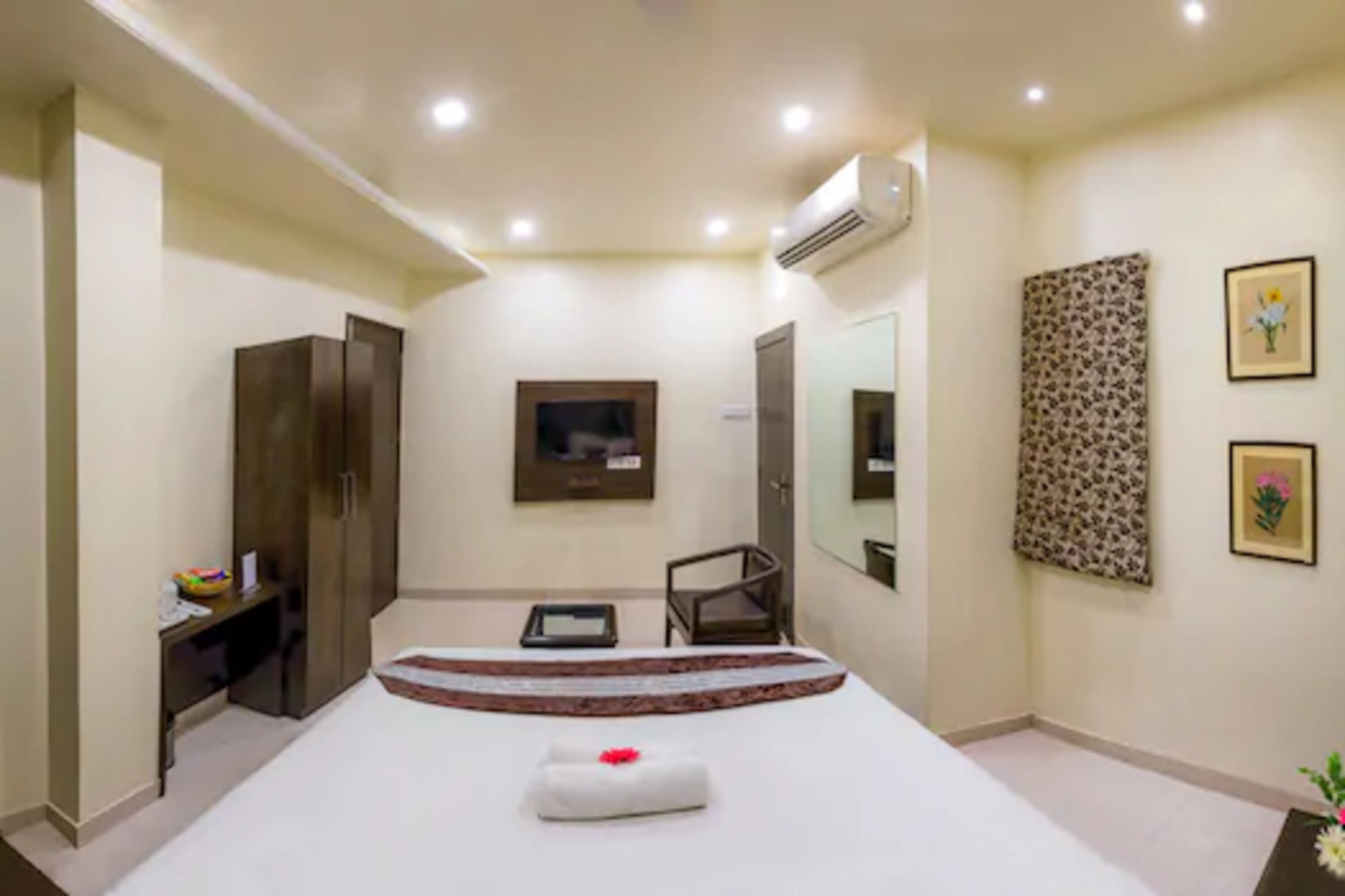 A hotel room with a bed, a desk, a chair, a wardrobe, a mirror, and a wall-mounted air conditioner.