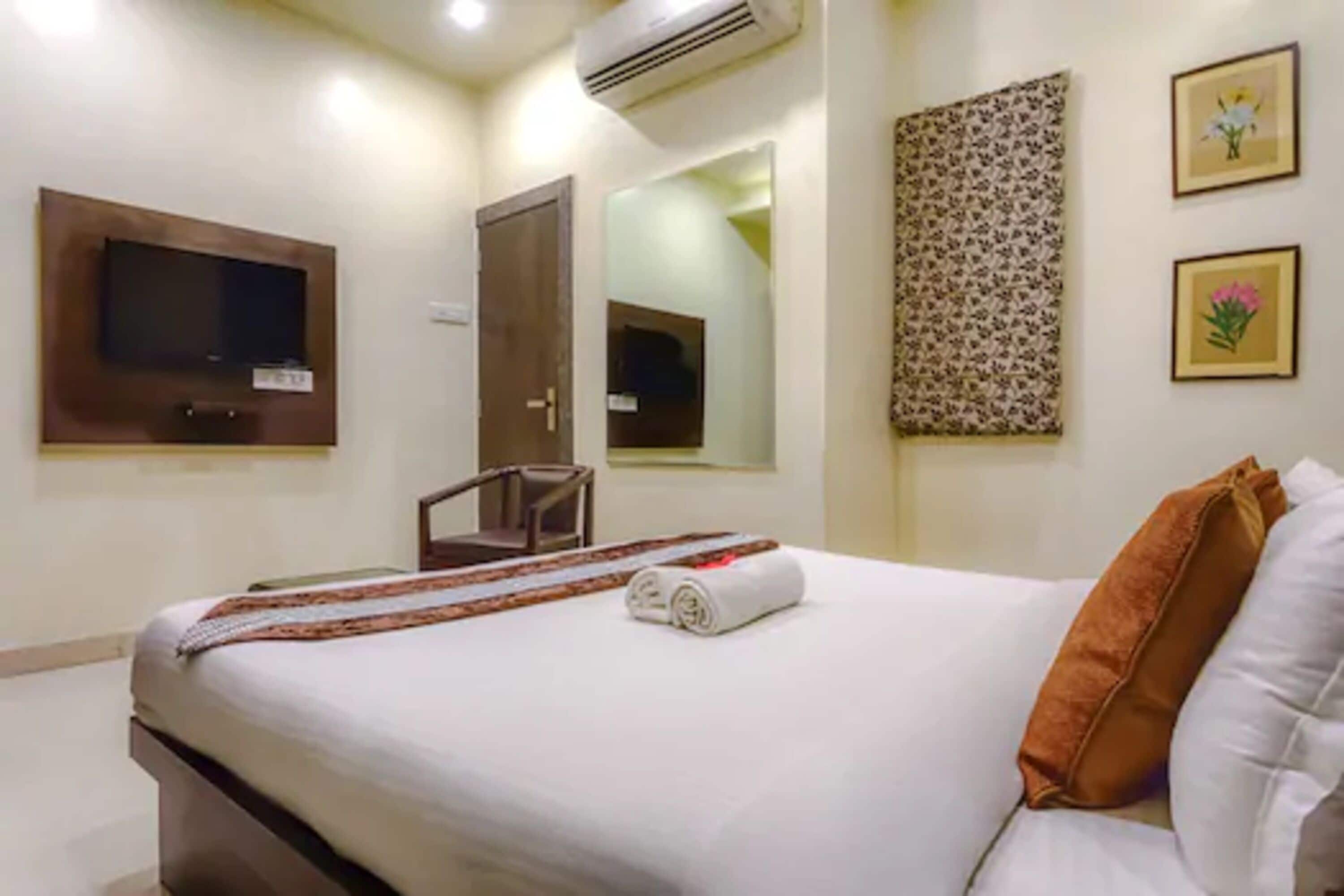 Une chambre d’hôtel avec un lit, un téléviseur fixé au mur, une chaise et un miroir.