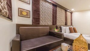 A room with a brown sofa, a bed with white and brown bedding, a decorative lantern, and framed pictures on the wall. - Hotel Imperial (Ajmer)