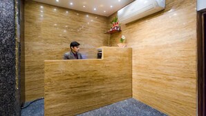 A reception area with a wooden reception desk, a wall-mounted air conditioner, and a small decorative plant. - Hotel Imperial (Ajmer)