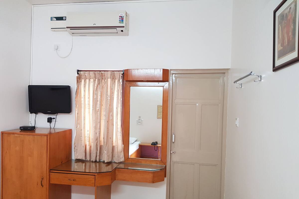 Una habitación con un escritorio de madera, televisor, espejo, armario y una puerta.
