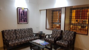 A living room with a patterned sofa, a coffee table with magazines, and a framed picture on the wall. - Sri Kumara Lodge (Bengaluru)