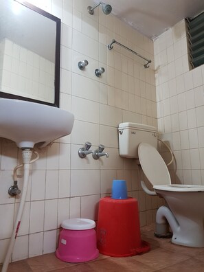 A bathroom with a white sink, toilet, and shower. There are two buckets, one pink and one red, on the floor. - Sri Kumara Lodge (Bengaluru)