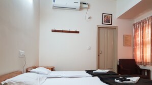 A bedroom with two beds, a wardrobe, a desk, and an air conditioning unit. - Sri Kumara Lodge (Bengaluru)