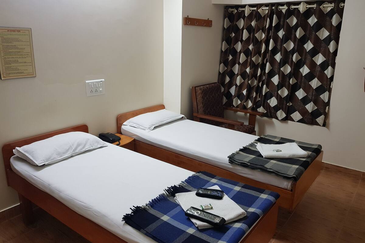 Habitación de hotel con dos camas individuales, cabecera de madera, mesita de noche pequeña con teléfono, manta y control remoto.