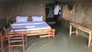 A tented accommodation room with a bed, a wooden bench, and a table. - Ruma River Lodge (Ndhiwa)