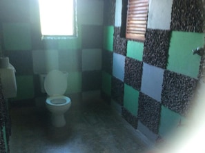 A bathroom with a checkered wall pattern, a toilet, and a window with blinds.