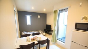 A compact dining area with a table, chairs, a clock, and a television. - Tenjin Higashi Russo (Fukuoka)