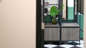 A room with a checkered floor, a plant on a table, and a door leading to another room.